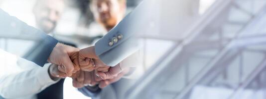 Cropped of a business teams hands clasped together in a fist bump, showcasing their camaraderie and unity. The image captures the essence of teamwork and collaboration in a professional setting. photo