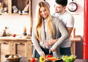 A young couple enjoys quality time as they prepare a nutritious meal in their warm, inviting kitchen. They share laughter while chopping fresh vegetables for a delicious dish. photo