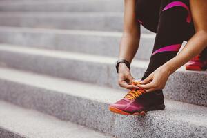Start jogging on street. African american girl in sportswear tying shoelaces on sneakers on stairs, free space, cropped photo