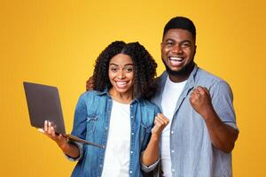 Excited young adults express joy and accomplishment, with one holding a laptop. Their vibrant expressions reflect happiness in a lively, yellow background, suggesting a moment of achievement. photo