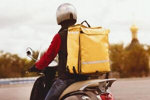 Fast Delivery. Courier Man With Yellow Backpack Delivering Meals On Scooter Outside. Rear View photo