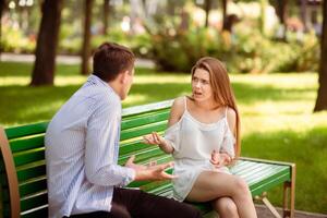 Relationship problems concept. Millennial couple having argument on bench at summer park photo