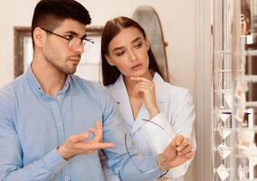 A man and woman are engaged in a discussion while examining various eyewear at a boutique. The stylish setting and attentive expressions highlight their decision-making process. photo