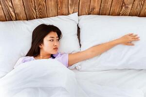 Depressed Asian Woman After Divorce Touching Empty Pillow Suffering From Loneliness Lying Alone In Bed In Bedroom After Breakup. Top-View photo