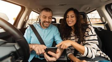 Short Road Route. Portrait of smiling couple sitting inside luxury car pointing fingers at smart phone, cheerful male driver holding cell, showing choosing location, using digital map application photo
