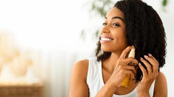Hair Care. Happy Afro Woman Using Oil For Split Ends While Getting Ready At Home, Closeup Image With Copy Space photo
