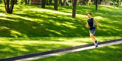 Fast run in park. Guy in sportswear jogging at track, on green lawn, free space photo