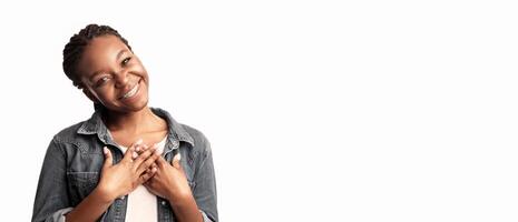 A young woman stands in a studio, smiling warmly while placing her hands over her heart, showcasing her expression of gratitude and joy in a bright and airy environment. photo