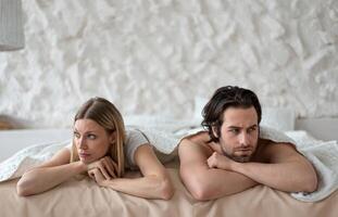 Sexual problems, relationship crisis. Stressed young couple lying in bed, overwhelmed with family difficulties, not speaking after conflict, suffering from erectile dysfunction or lack of libido photo