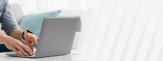 Unrecognizable man working on pc, typing text or programming code on computer keyboard, sitting on sofa at home, cropped, empty space. Busy entrepreneur photo
