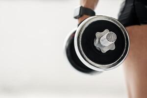 Exercises for muscle and heart rate tracking. Middle aged woman athlete in sportswear and fitness tracker hold dumbbell in interior of gym or home, close up, free space, cropped, studio shot photo