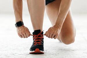 Preparation for marathon. Woman with smart watch tying shoelaces on sneakers, sitting on floor in gym or living room, panorama, copy space photo