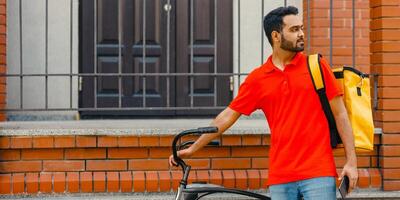 Courier with bicycle, delivery food service at home. Man with beard with mobile phone finds address in city, free space photo
