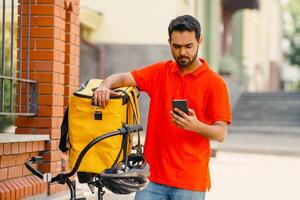 Eco transport and fast food delivery in city. Young male cyclist in protective gear with yellow bag on street, looking customer address, copy space photo