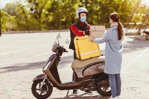 Courier Service. Delivery Man Giving Woman Food Boxes With Lunch Ordered In Restaurant Standing With Scooter, Wearing Protective Mask Outside photo