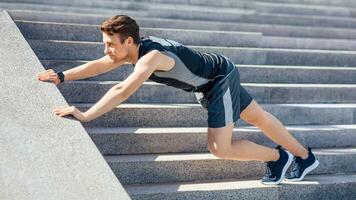 Outdoor workout. Guy in sport uniform, with fitness tracker doing exercises on stairs, profile, free space photo