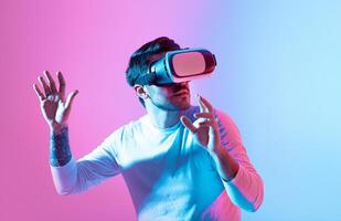 A man interacts with virtual reality technology, wearing a VR headset while standing against a colorful backdrop. His hands are raised as he explores immersive digital environments. photo
