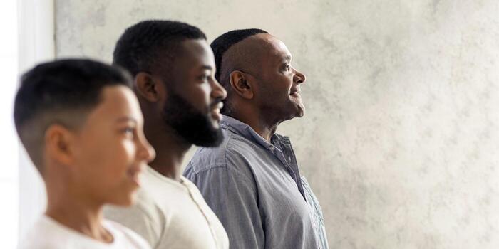 Three generations of men stand together, each representing different ages and experiences, sharing a moment of connection and reflection in a bright indoor space. photo