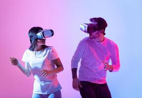 Two individuals engage in a virtual reality activity, wearing headsets and laughing as they navigate an immersive digital world, illuminated by colorful lighting. photo