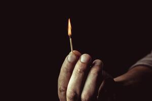 Playing with fire. A burning match in a man's hand on a black background. photo