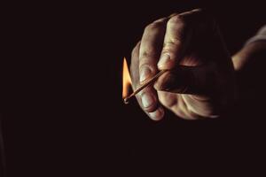 Playing with fire. A burning match in a man's hand on a black background. photo