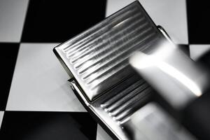 Close-up view of a chrome foot pedal on a checkerboard surface in a workshop photo