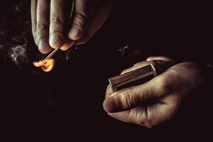 Playing with fire. A burning match in a man's hand on a black background. photo