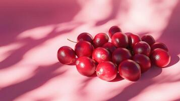 A cluster of vibrant red fruits rests on a soft pink surface, with gentle shadows creating an artistic contrast. The warm afternoon light enhances the fresh appearance of the fruits photo