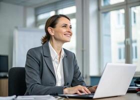 a woman in a business suit is smiling while using a laptop photo