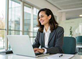 a woman in a business suit is smiling while using her laptop photo