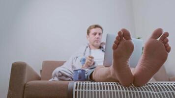 A freelance man works from home during the energy crisis, wrapped in a warm blanket and enjoying hot tea. video