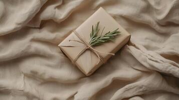 A gift box wrapped in brown paper and tied with twine sits elegantly on a light, textured fabric. Fresh herbs add a natural touch to the presentation photo