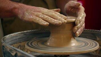 Close up unrecognizable Caucasian man guy small business owner potter craftsman male hands shaping wet clay mud on spinning circle rotating wheel making pottery artwork vase indoor workshop art studio video