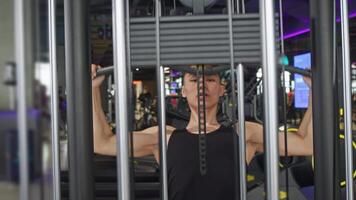 Man engages in physical activity at gym, utilizing device that aids in development of muscular strength in his arms. simulator entails lifting of metal weights with wide grip. video
