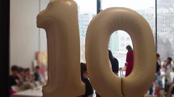 Party being held in school classroom to celebrate anniversary of one of students. In foreground, there are inflated balloons hanging with number 10 on them. video