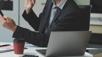 A man in a suit is using his phone while sitting at a desk video