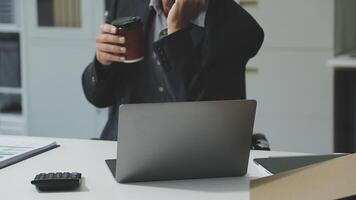 A man in a suit is sitting at a desk with a laptop and a cup of coffee video