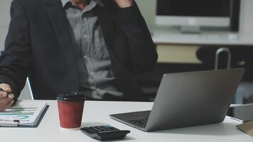 A man in a suit sitting at a desk with a laptop video