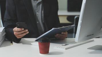 A man in a suit is using his phone while sitting at a desk video