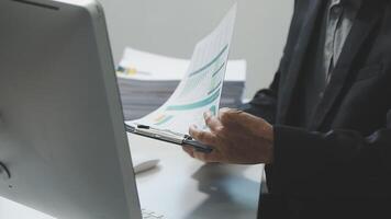 A man in a suit is holding a piece of paper and looking at a computer screen video