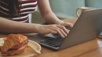A woman typing on her laptop while holding a croissant video