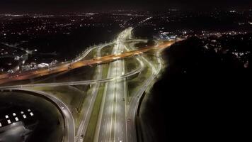 Illuminated highway interchange at night, aerial view of modern road infrastructure with light trails and cityscape, urban transportation network in motion video