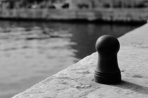 A mooring post by the water's edge in black and white. photo