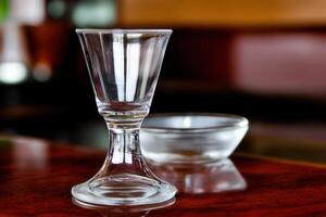 A clear glass shot glass beside a small dish. photo