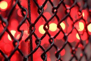 Close-up of a chain-link fence with red bokeh lights. photo