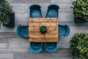 A wooden table surrounded by blue chairs and plants. photo
