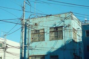 A weathered blue building with power lines against a clear sky. photo
