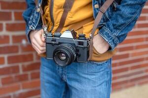Person holding a vintage camera against a brick wall. photo
