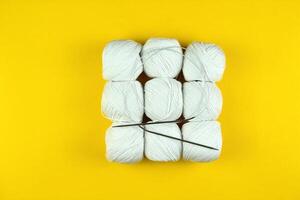 On a yellow background lies white yarn for knitting and knitting needles. Square figure. Business concept photo