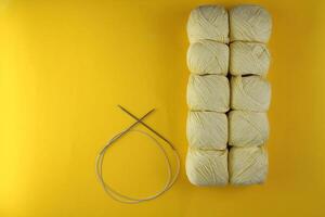 Ten skeins of yellow yarn with knitting needles on a yellow background photo